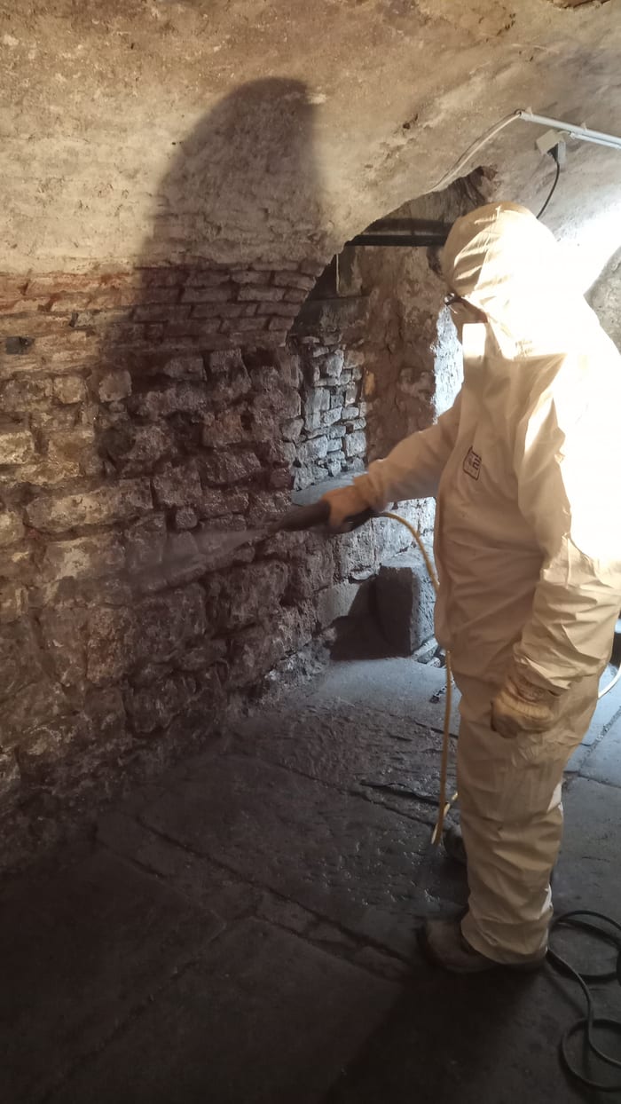Fachkraft im weißen Schutzanzug beschäumt eine Kellerwand mit Fungizid zur Bekämpfung des Echten Hausschwamms, Raum Schwäbisch Hall